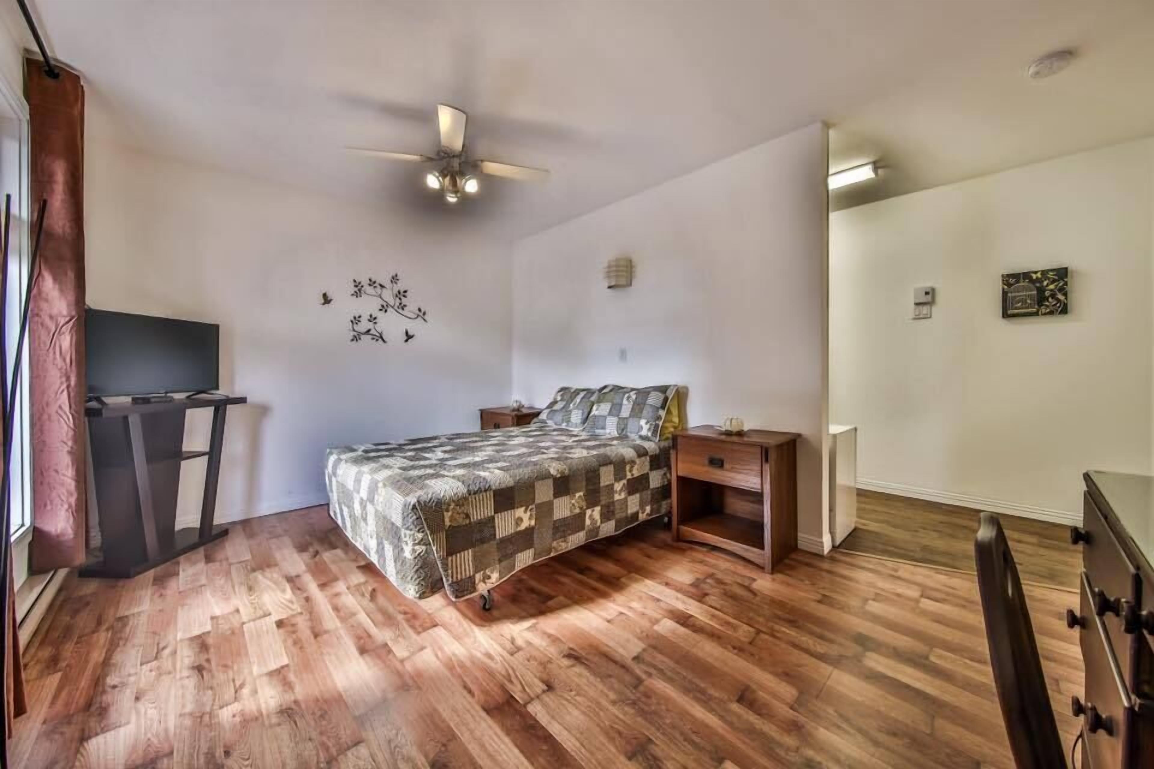 A bedroom with a bed, wooden flooring, a ceiling fan, a desk, and a chair.