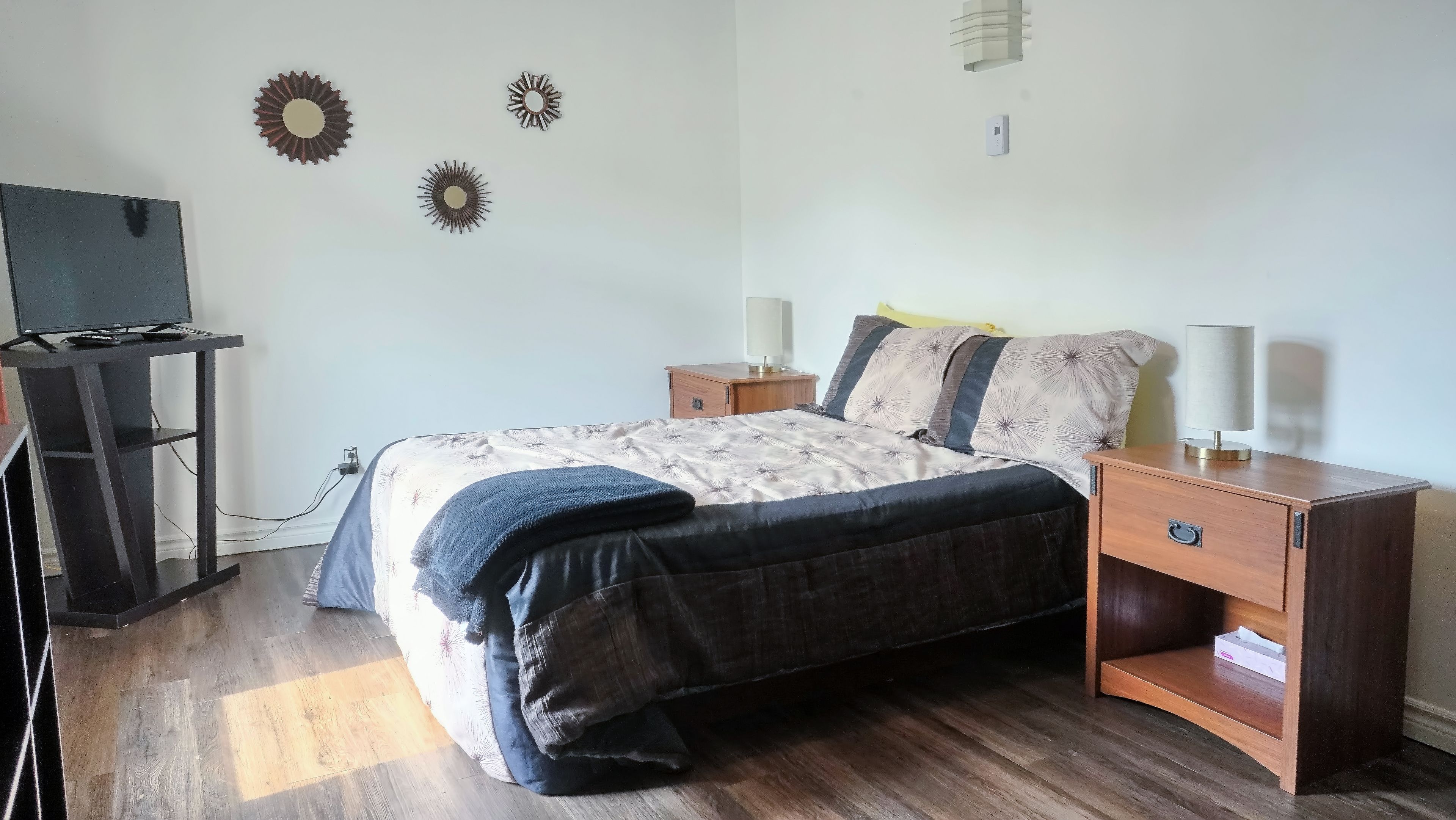 A bedroom with a bed, bedside tables, a TV stand, and wall decorations.