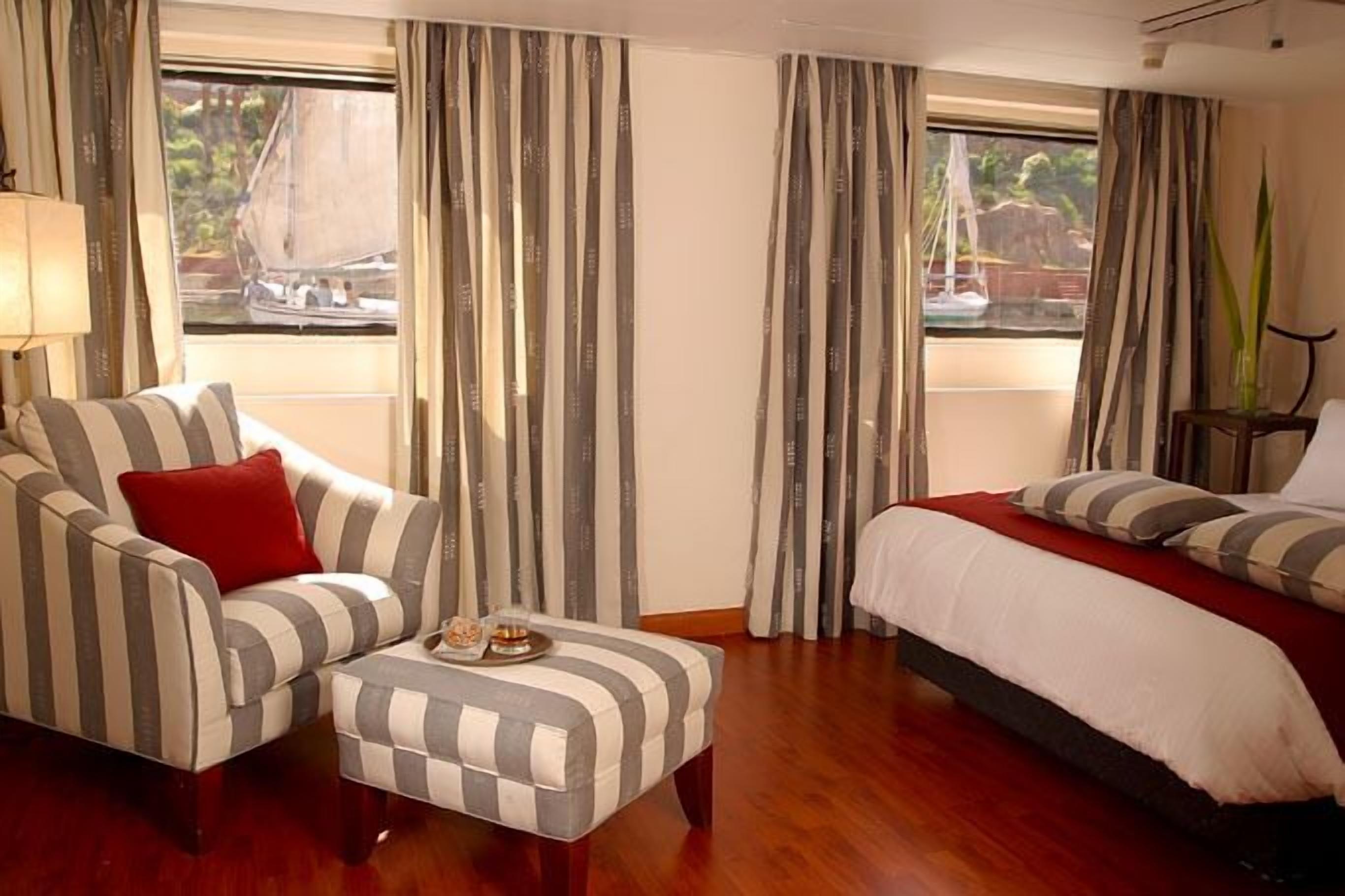 Una habitación de hotel con un sofá a rayas, un pequeño otoman, una cama con ropa de cama a rayas y cortinas.