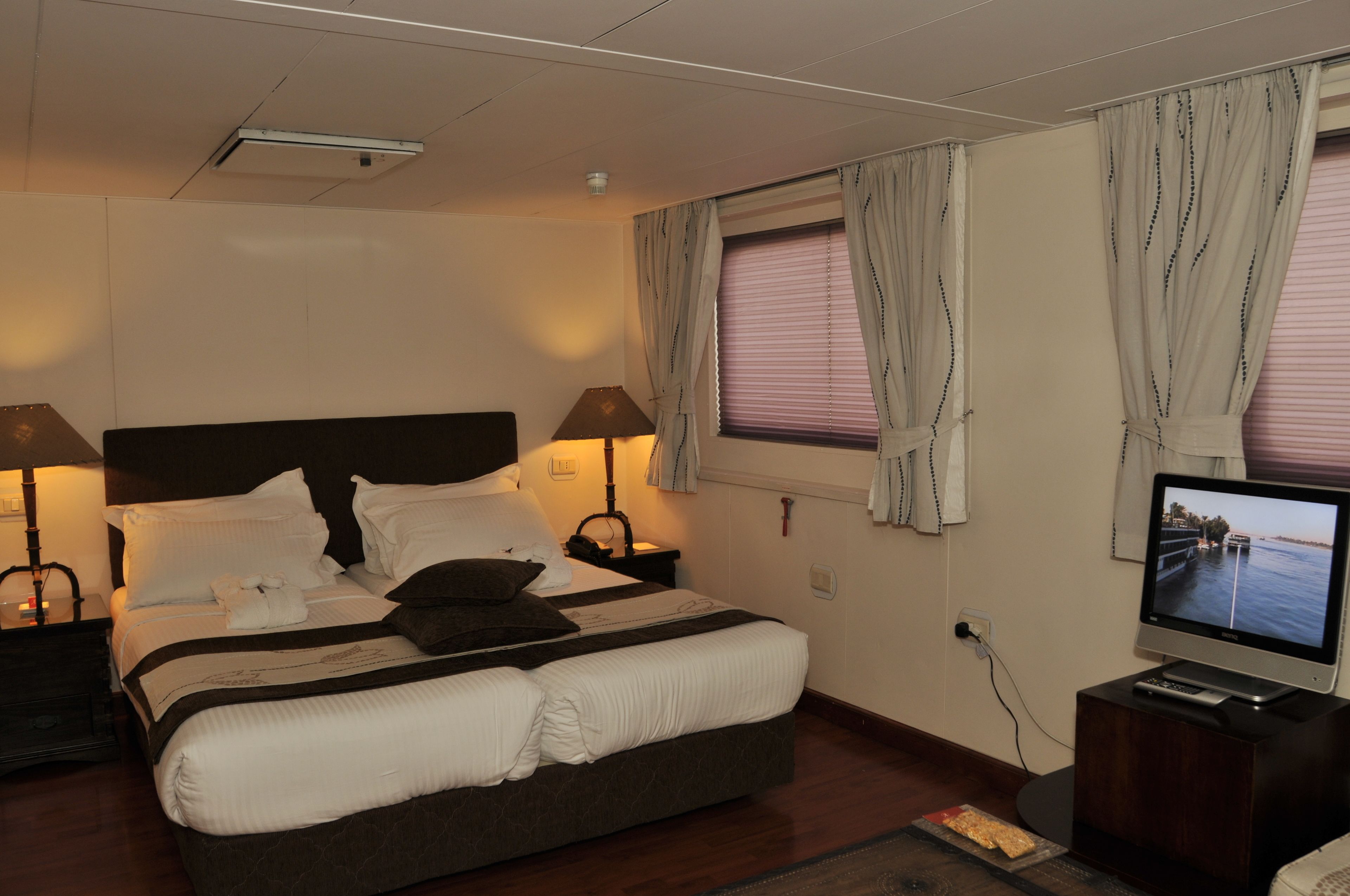 Ein Hotelzimmer mit einem großen Bett, zwei Nachttischlampen, einem Fernseher auf einem Tisch und einem fenster mit Vorhängen.