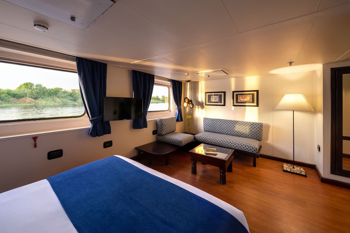 A room with a bed, two patterned sofas, a small table, a lamp, and a window with curtains.