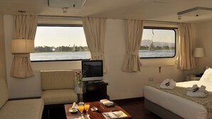 Habitación de hotel con cama, sofá, televisor, una mesa de centro con bebidas y vistas al agua.