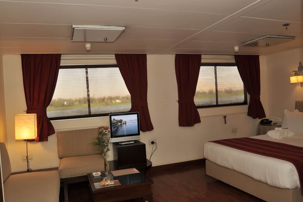 A hotel room with a bed, a TV on a stand, a bedside table with a lamp, and a window with curtains.