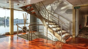 Un interior moderno con una escalera de caracol, grandes ventanales con vistas a un cuerpo de agua y un extintor en la pared.