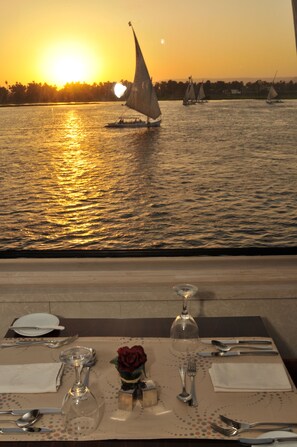 A table set for two with a view of sailboats on the water during sunset. - MS Alexander The Great Nile Cruise (Luxor)