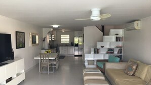 A modern living room with a sofa, a TV, and a dining area with chairs and a table. - Villa 415A at Jolly Harbour (Jolly Harbour)