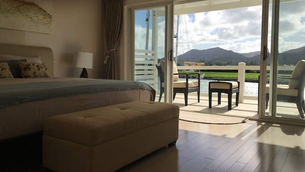 A bedroom with a large bed, a sofa, and a view of a body of water and mountains through a sliding glass door. - Villa 415A at Jolly Harbour (Jolly Harbour)
