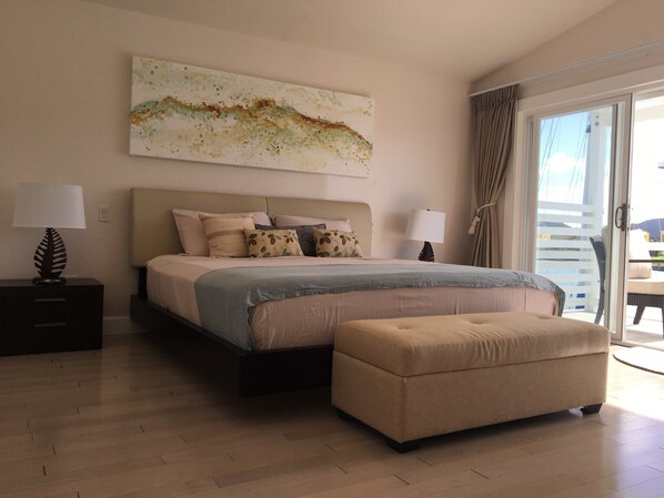 A bedroom with a bed, bedside tables, a large window, and a balcony. - Villa 415A at Jolly Harbour (Jolly Harbour)