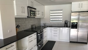 A modern kitchen with white cabinets, a black countertop, stainless steel appliances, and a black rug. - Villa 415A at Jolly Harbour (Jolly Harbour)