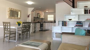 A modern living room with a sofa, a coffee table, and a dining area with chairs and a table. There is a kitchen in the background with cabinets and a microwave. - Villa 415A at Jolly Harbour (Jolly Harbour)