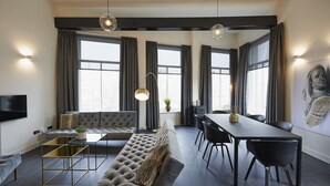 Una sala de estar moderna con un sofá, una mesa de centro, una mesa de comedor con sillas y un televisor montado en la pared.