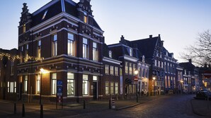 Un edificio histórico con un llamativo letrero 'DE BANK', amplias ventanas y un estilo arquitectónico europeo tradicional.