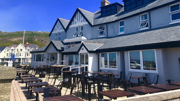 A row of seaside cottages with outdoor seating, large windows, and a clear view of the sea. - The Lilly (Llandudno)
