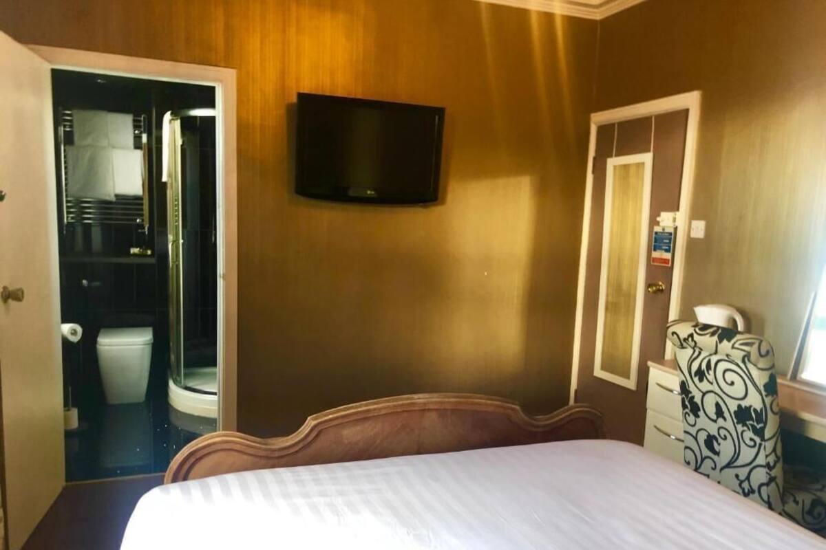 A hotel room with a bed, a television, a bathroom with a toilet and shower, and a dresser.