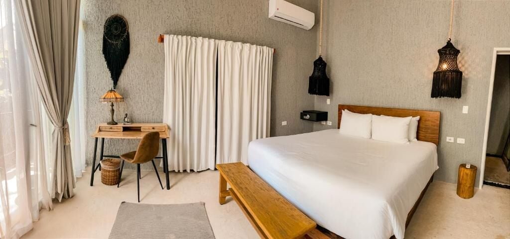 Une chambre à coucher comprenant un lit, un bureau, une chaise, un banc et deux lampes suspendues.