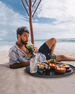 A person relaxing on a beach with a tray of food and drinks. - Hotelito Azul - A Michelin Key Winner (Tulum)