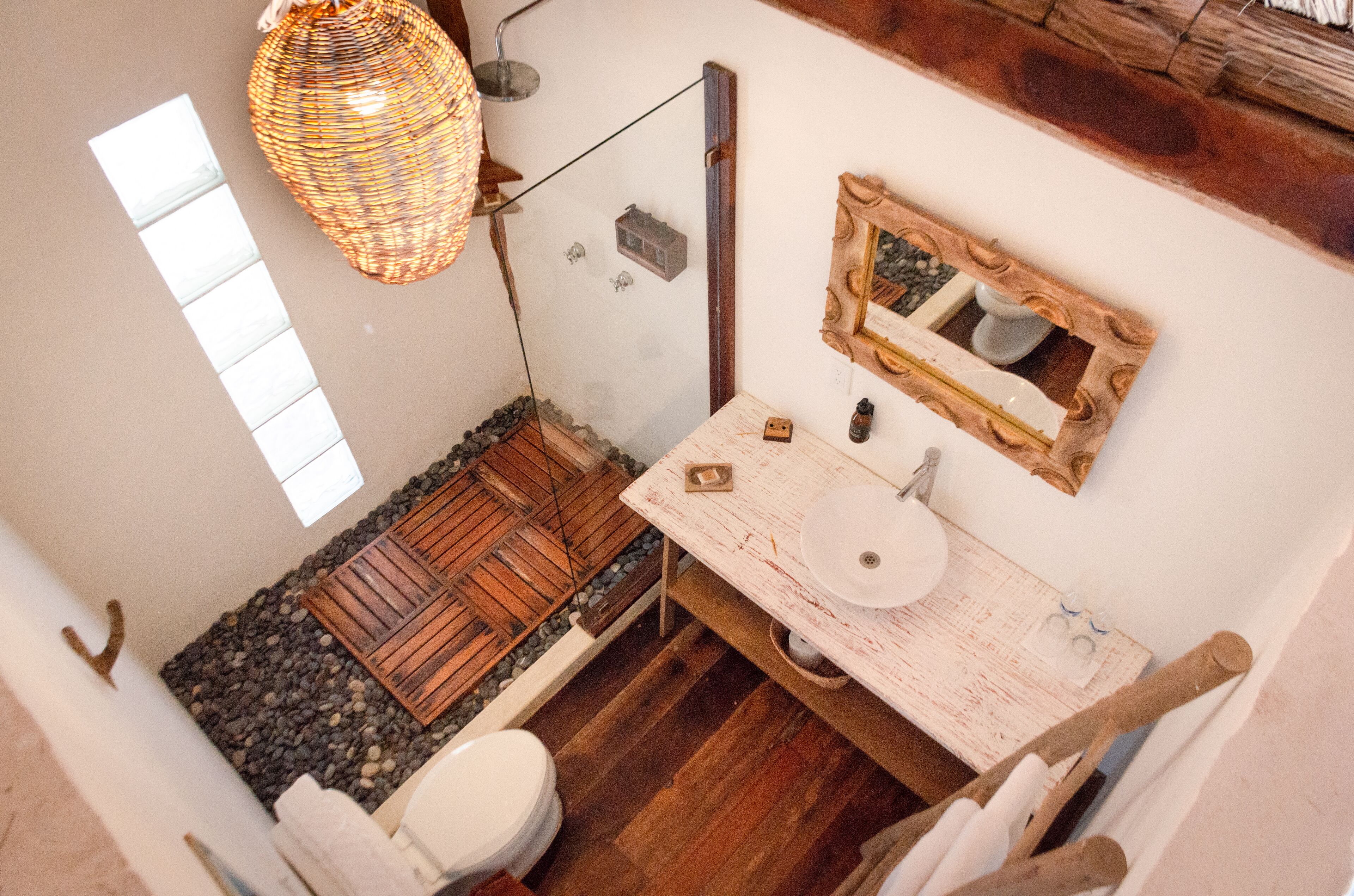 Une salle de bain avec un plancher en bois, un lavabo blanc, un miroir et un luminaire suspendu.