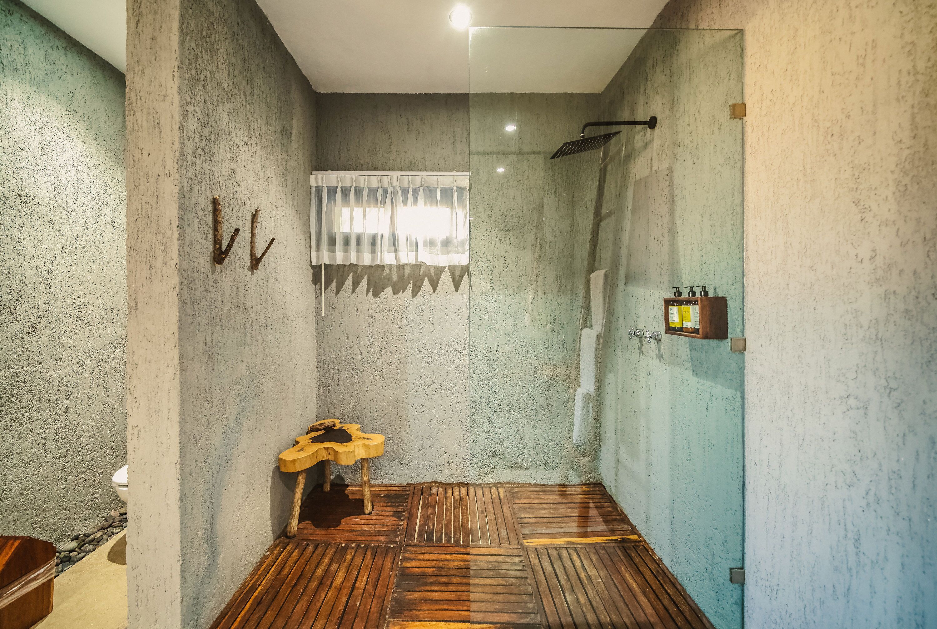 A bathroom with a concrete wall, a wooden floor, a shower, and a small wooden stool.