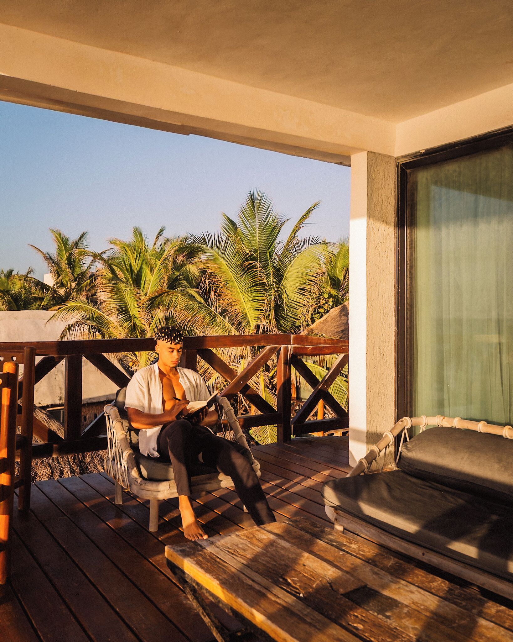 A wooden deck with a person sitting on a chair, a table, and a view of palm trees.