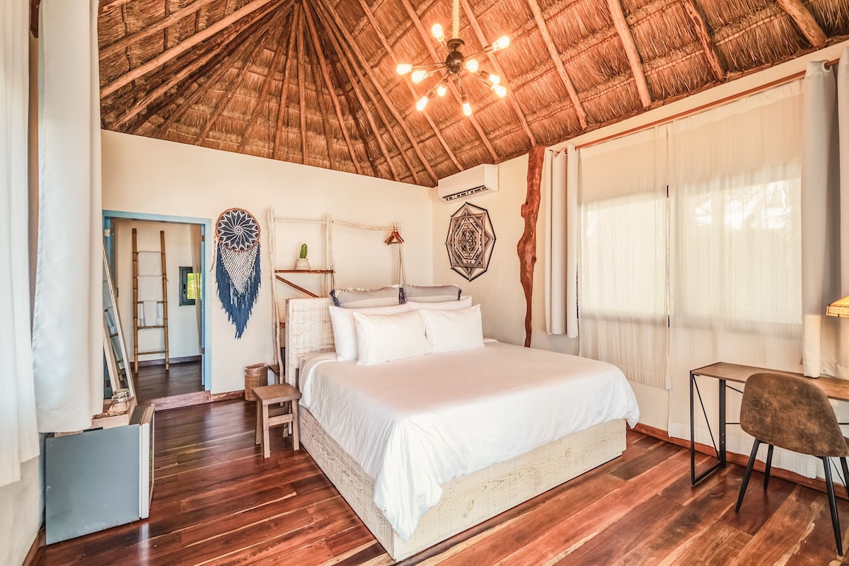 A bedroom with a wooden ceiling, a bed, a desk, and a chair.