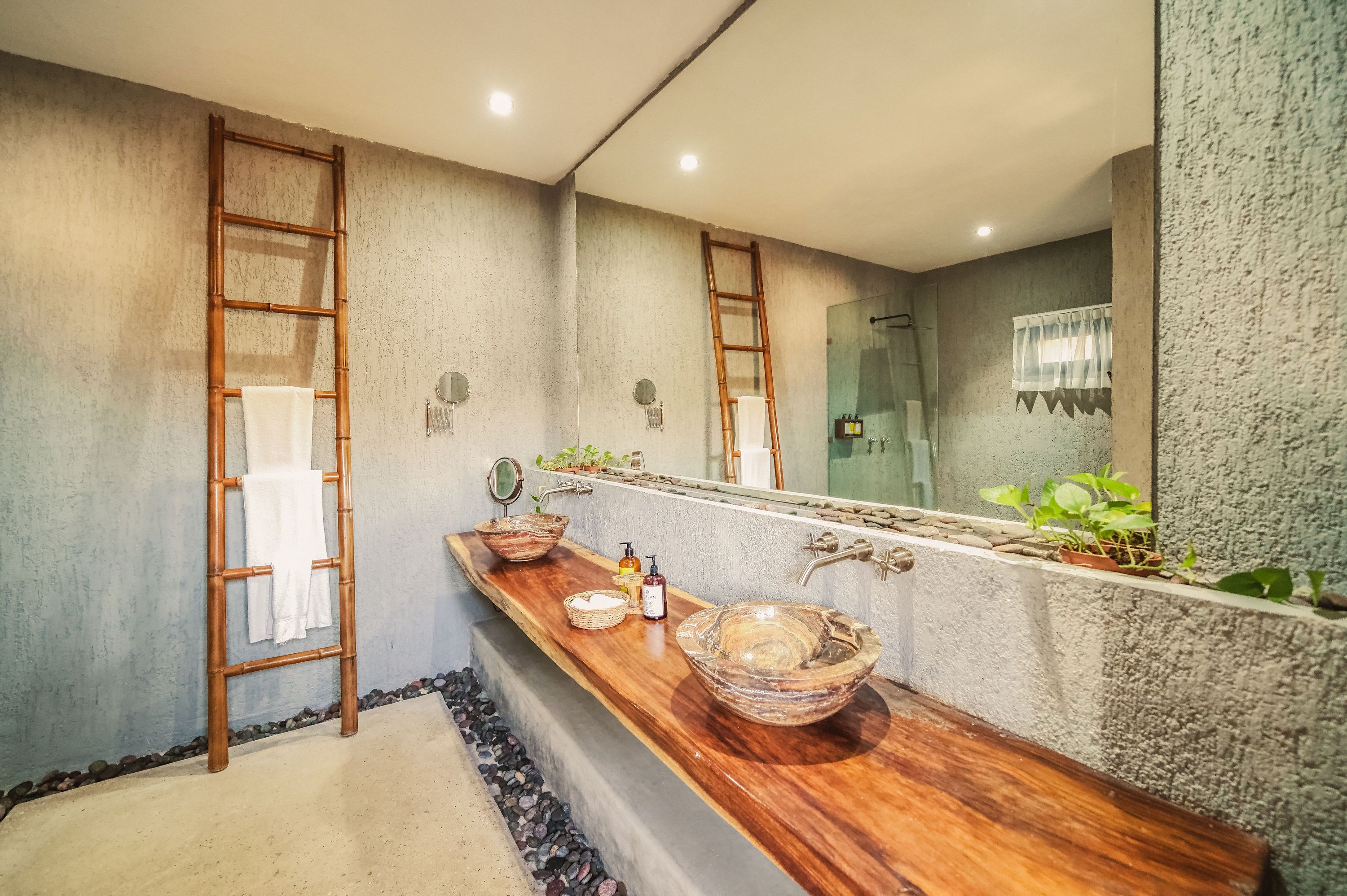 Un baño con tocador de madera, dos lavamanos de cerámica grandes, un espejo y zona de ducha.