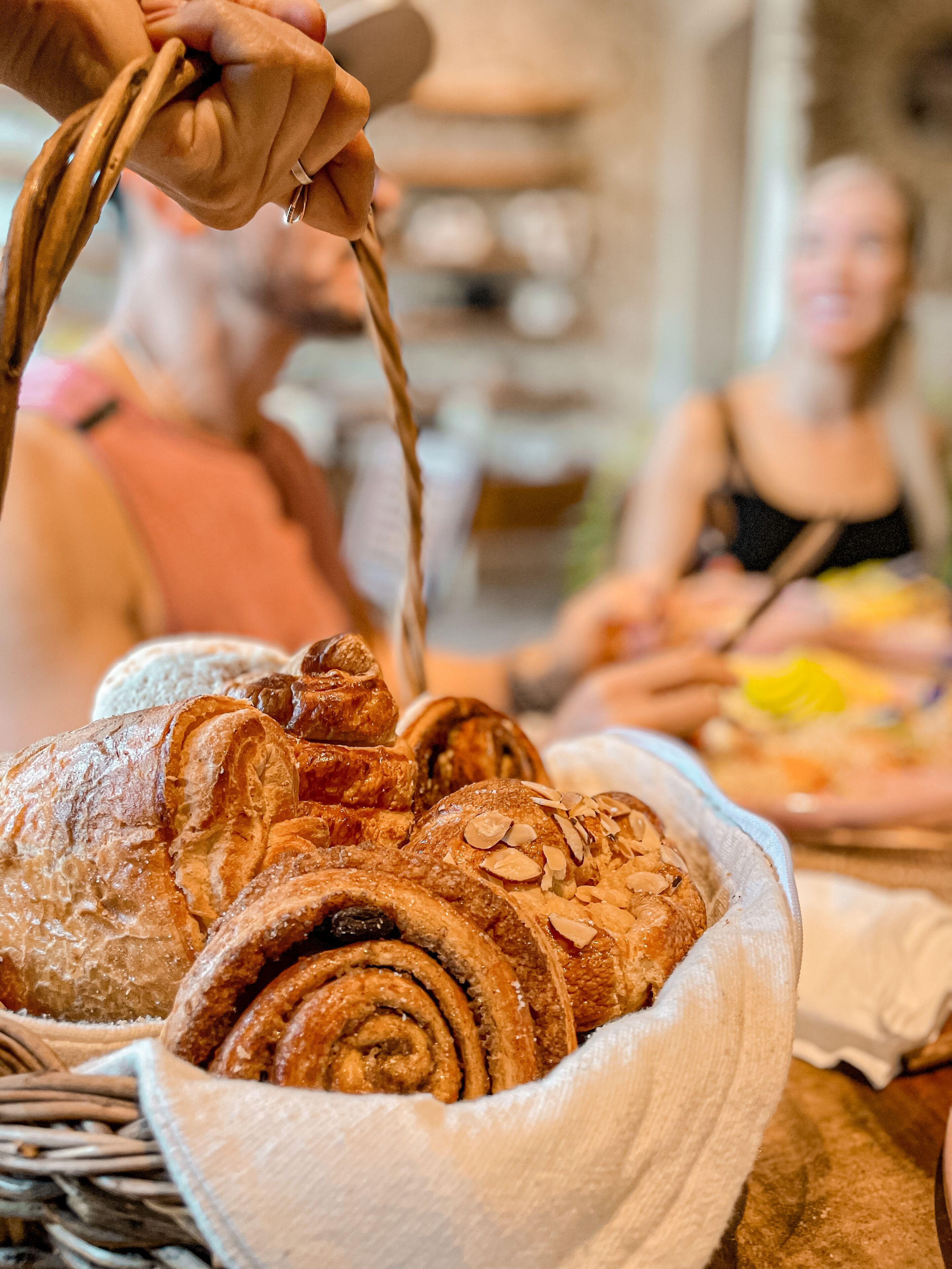 Pöydällä on kori täynnä leivonnaisia, kuten croissantteja ja kanelipullia.