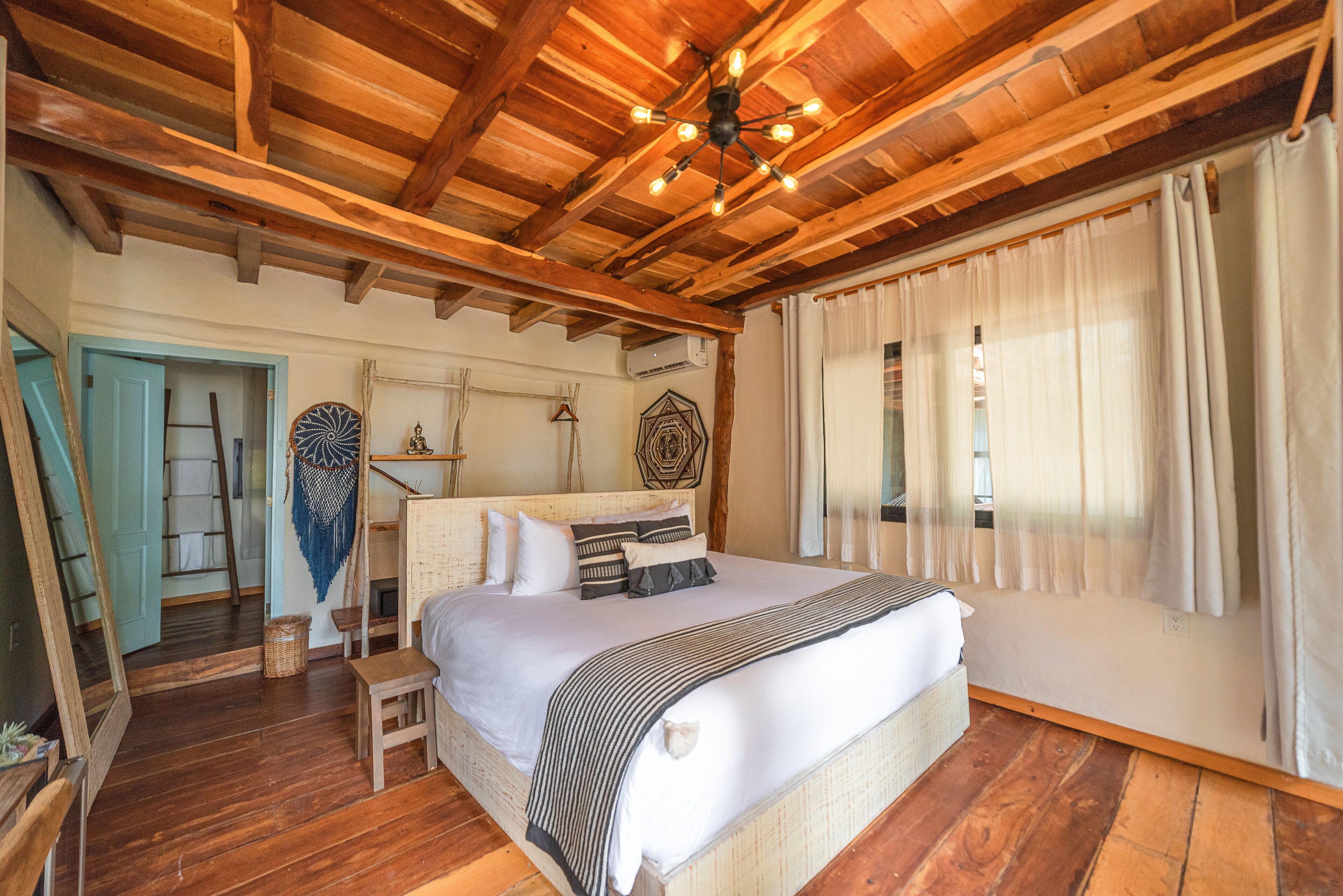 Um quarto espaçoso com uma cama grande, vigas de madeira no teto e um lustre.