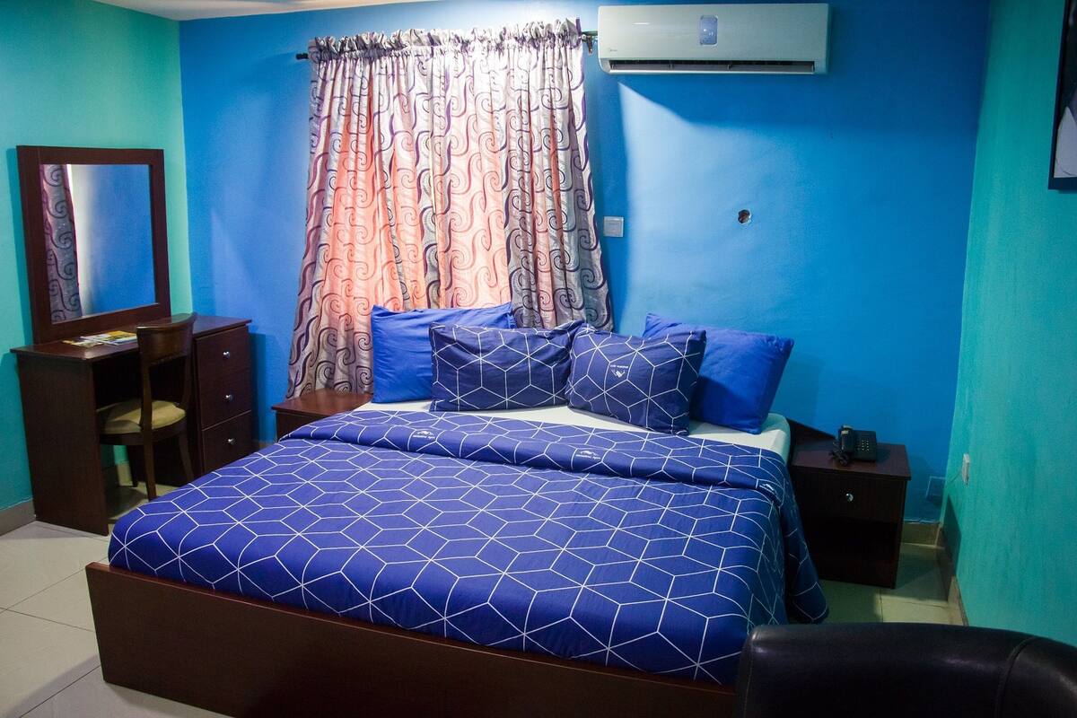 A bedroom with a bed, a nightstand, a dresser, a chair, and an air conditioning unit.