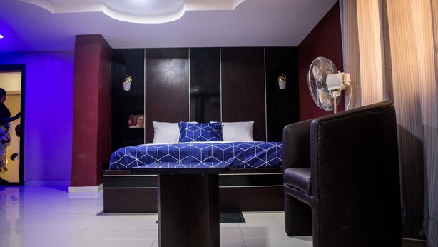 A modern bedroom with a bed, a desk, a chair, and a standing fan. - November 5 Hotel Lagos (Lagos)