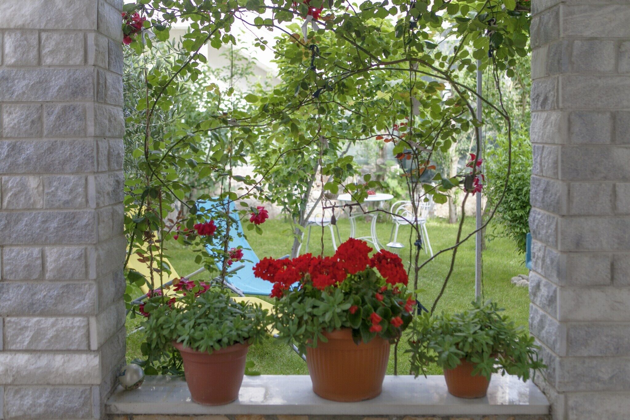 A stone wall with potted plants and a view of a grassy area with a blue chair.