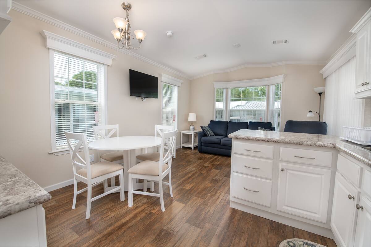 A modern kitchen with white cabinetry, a dining area with a white table and chairs, and a dark-colored sofa in the living area.