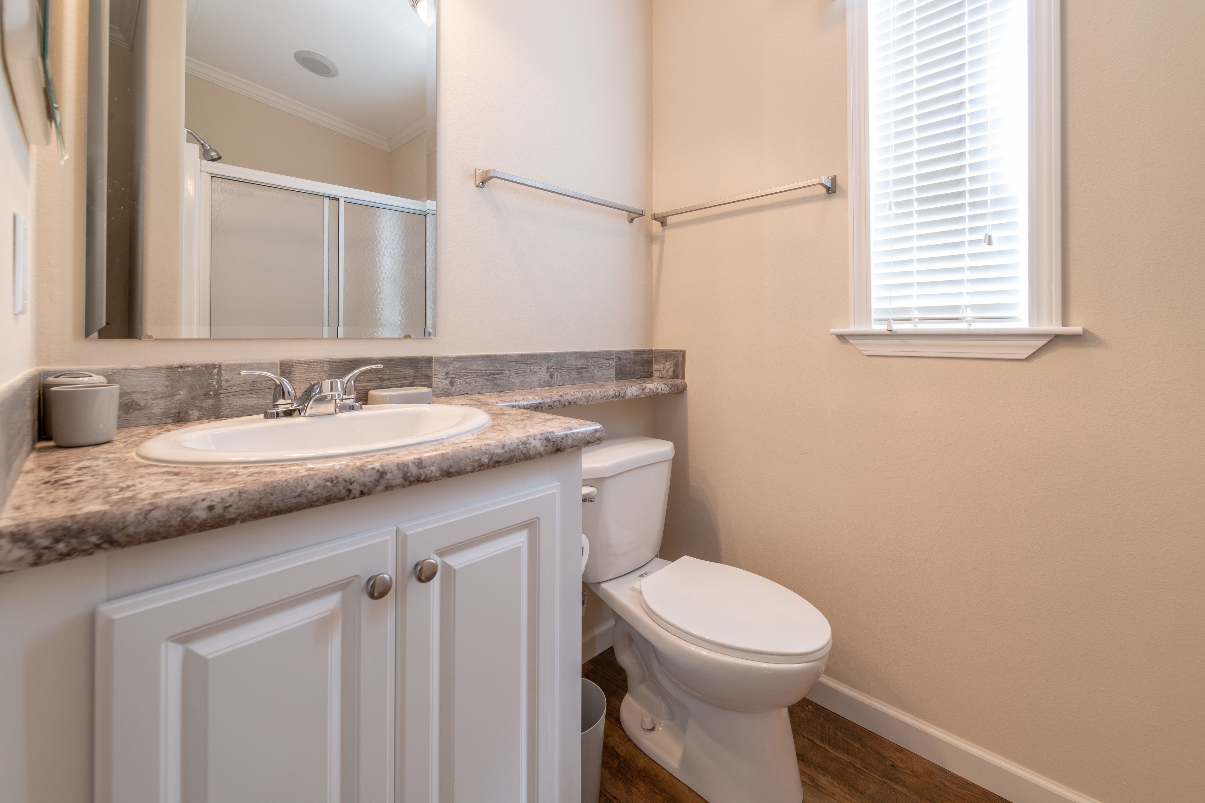 A bathroom with a white sink, a mirror, a toilet, and a window with blinds.