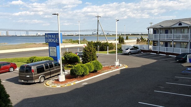 A parking lot with a sign for Royal Lodge, a building with balconies, and a view of a bridge and city skyline. - Royal Lodge (Absecon)