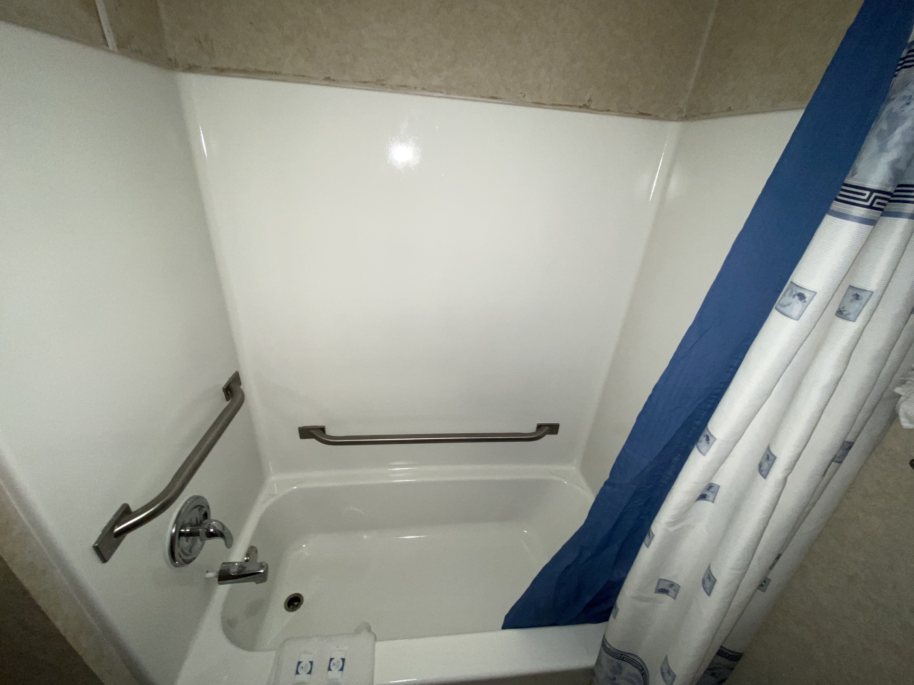 Un baño con bañera, barras de apoyo y cortina de ducha.