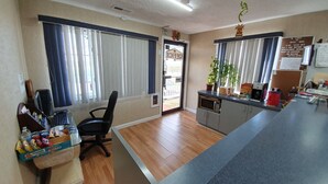 A hotel room with a kitchenette, a dining area with a chair and a table, a large window with curtains, and a door leading outside. - Royal Lodge (Absecon)