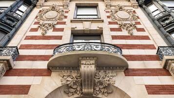 A building facade with ornate architectural details, including a central balcony with a wrought iron railing and decorative stone carvings.