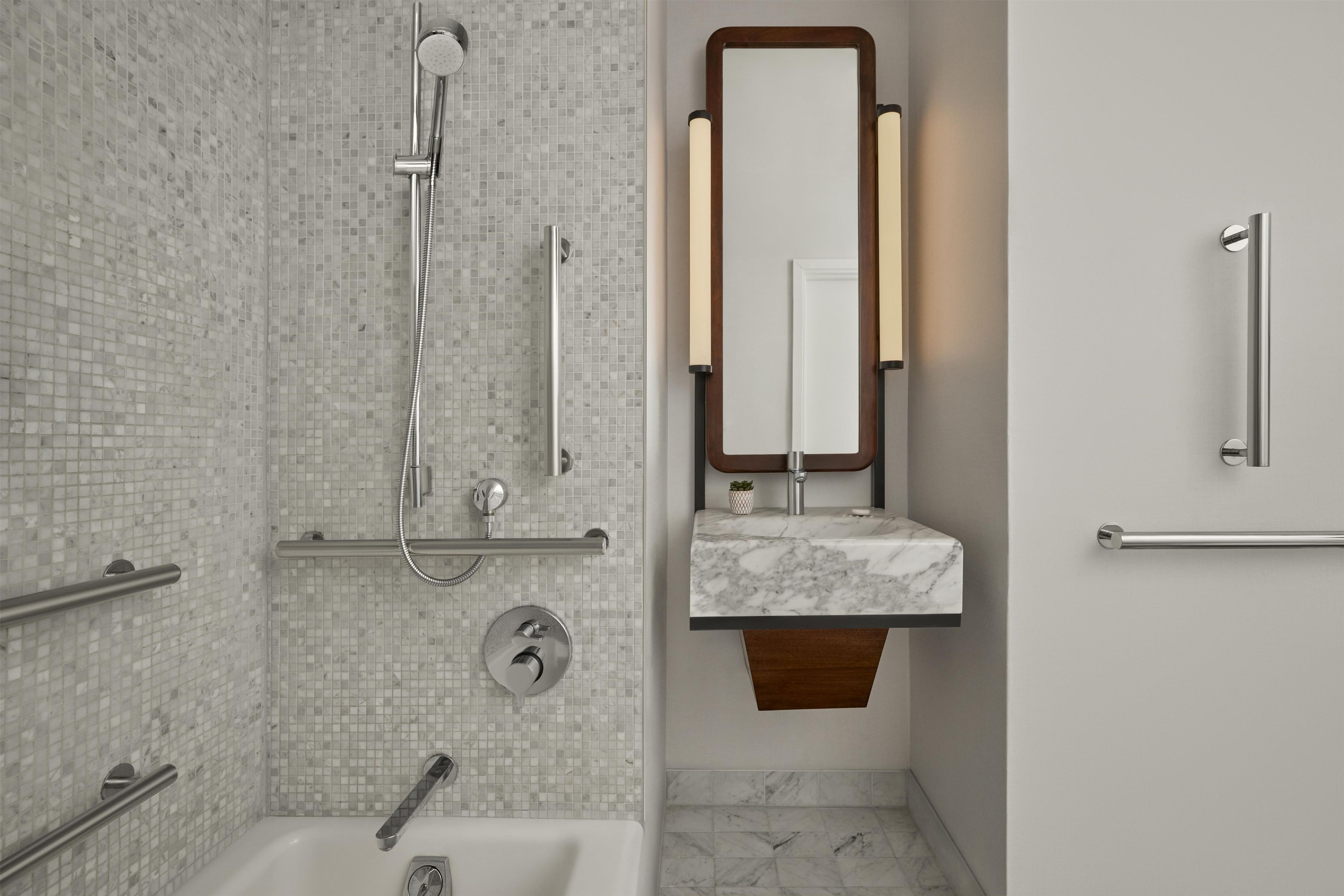A modern bathroom with a glass mosaic shower, a marble sink, and a wooden vanity.