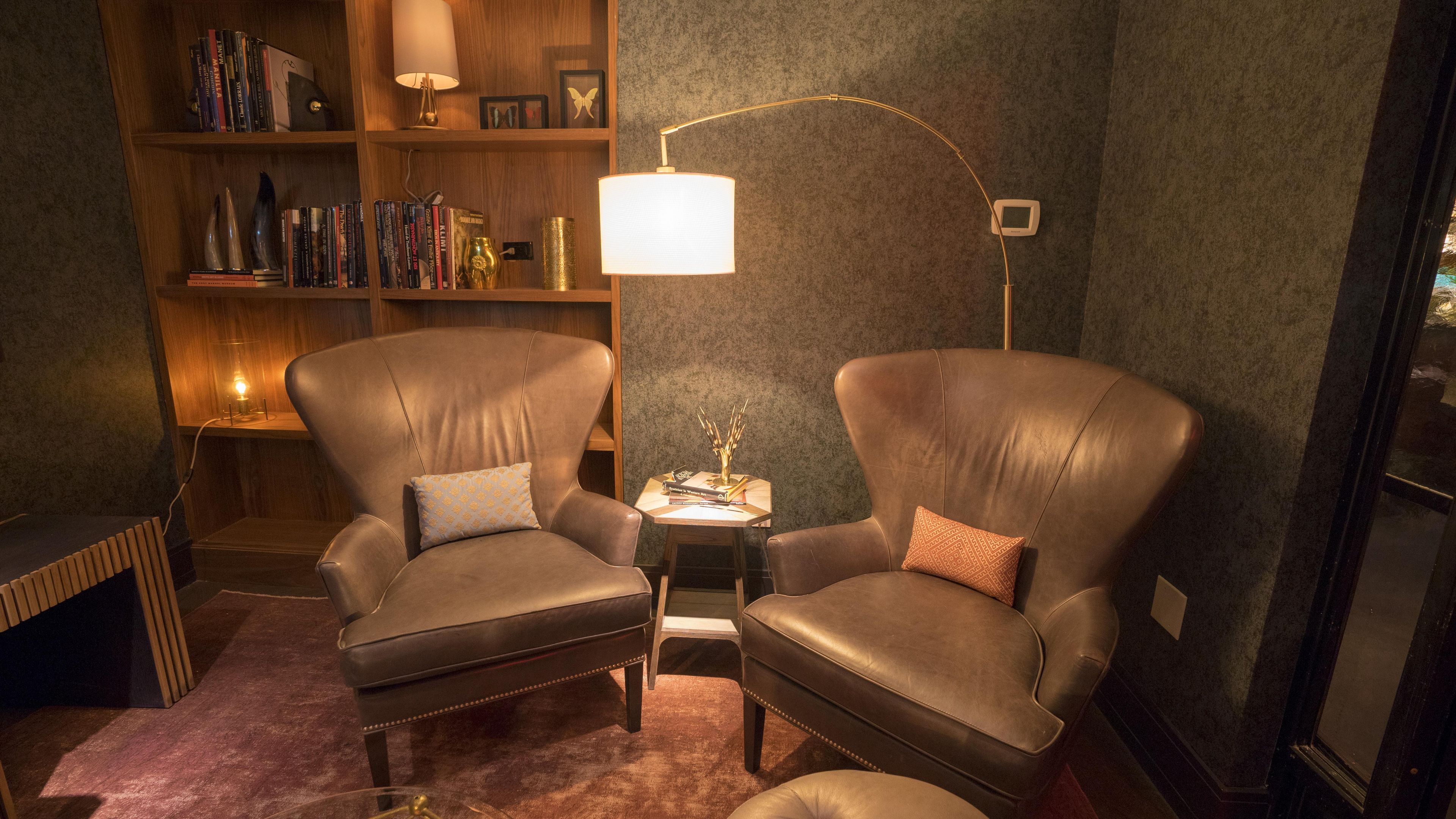 A room with two leather armchairs, a small table, a lamp, a bookshelf, and a radiator.