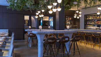 Un espace bar doté d’un comptoir en marbre, de tabourets en bois, de luminaires suspendus et d’un bar bien garni de bouteilles.