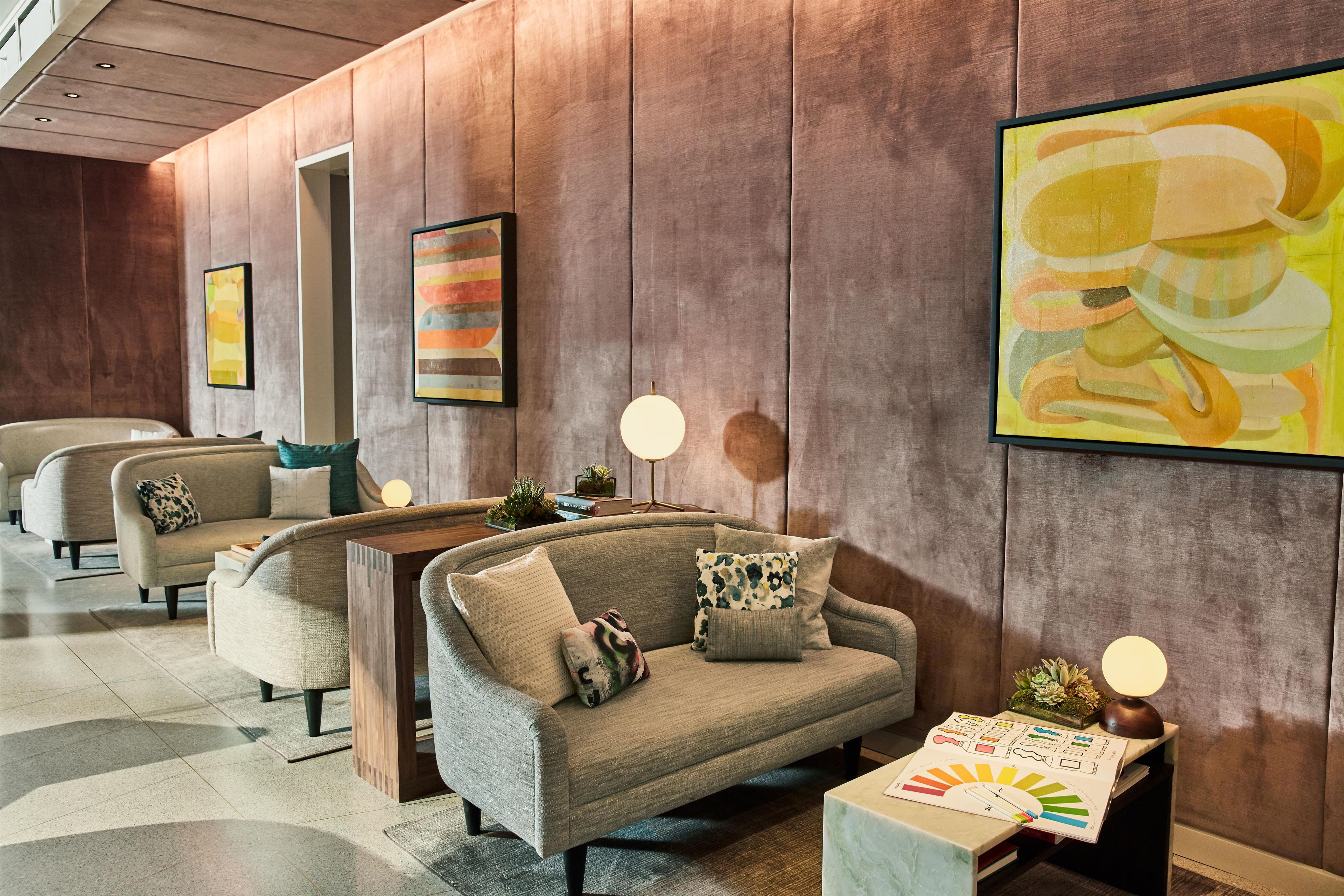 A modern lobby with a sofa, armchairs, and a coffee table. There are wall-mounted lamps and framed artwork.
