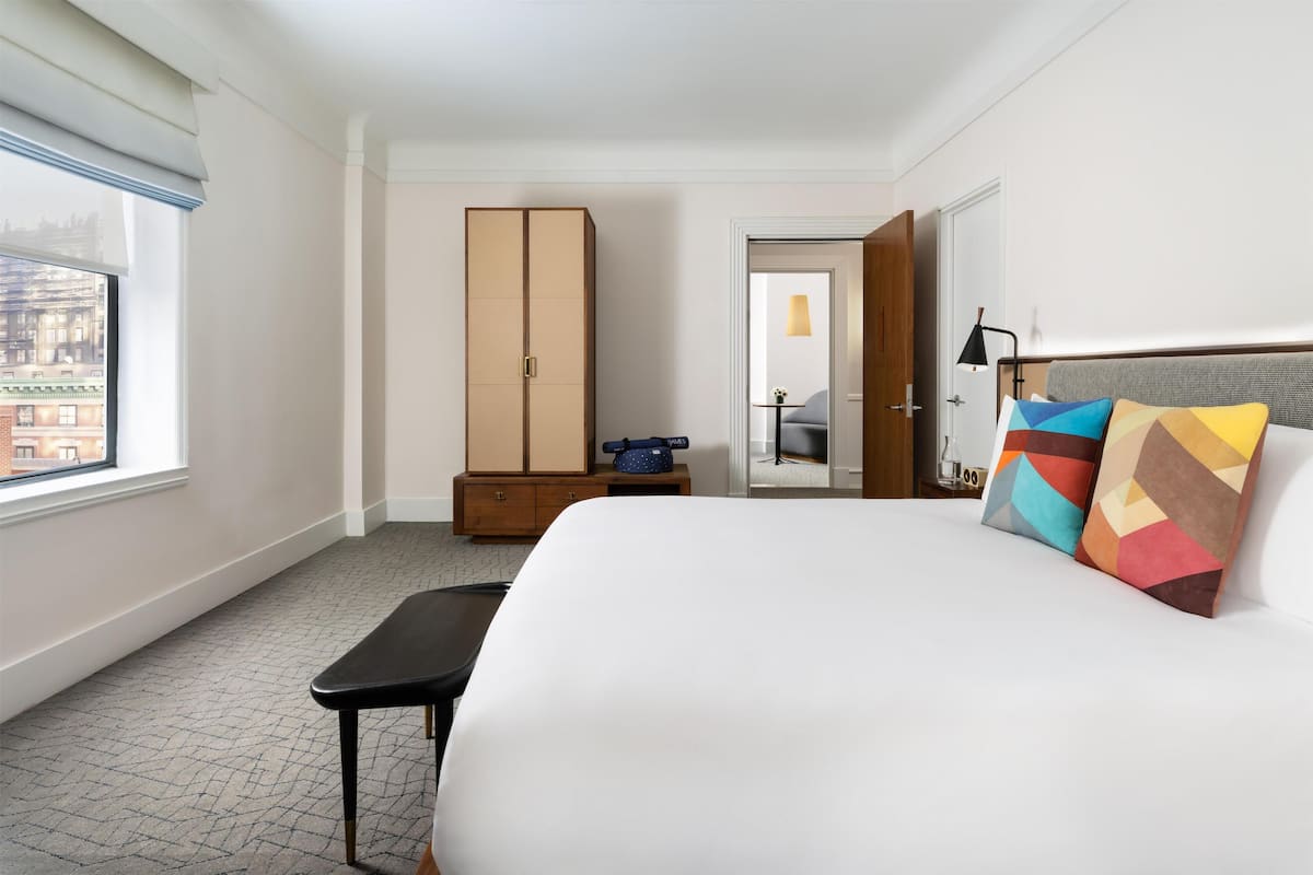 A hotel room with a large bed, a wardrobe, a desk, and a window with a city view.