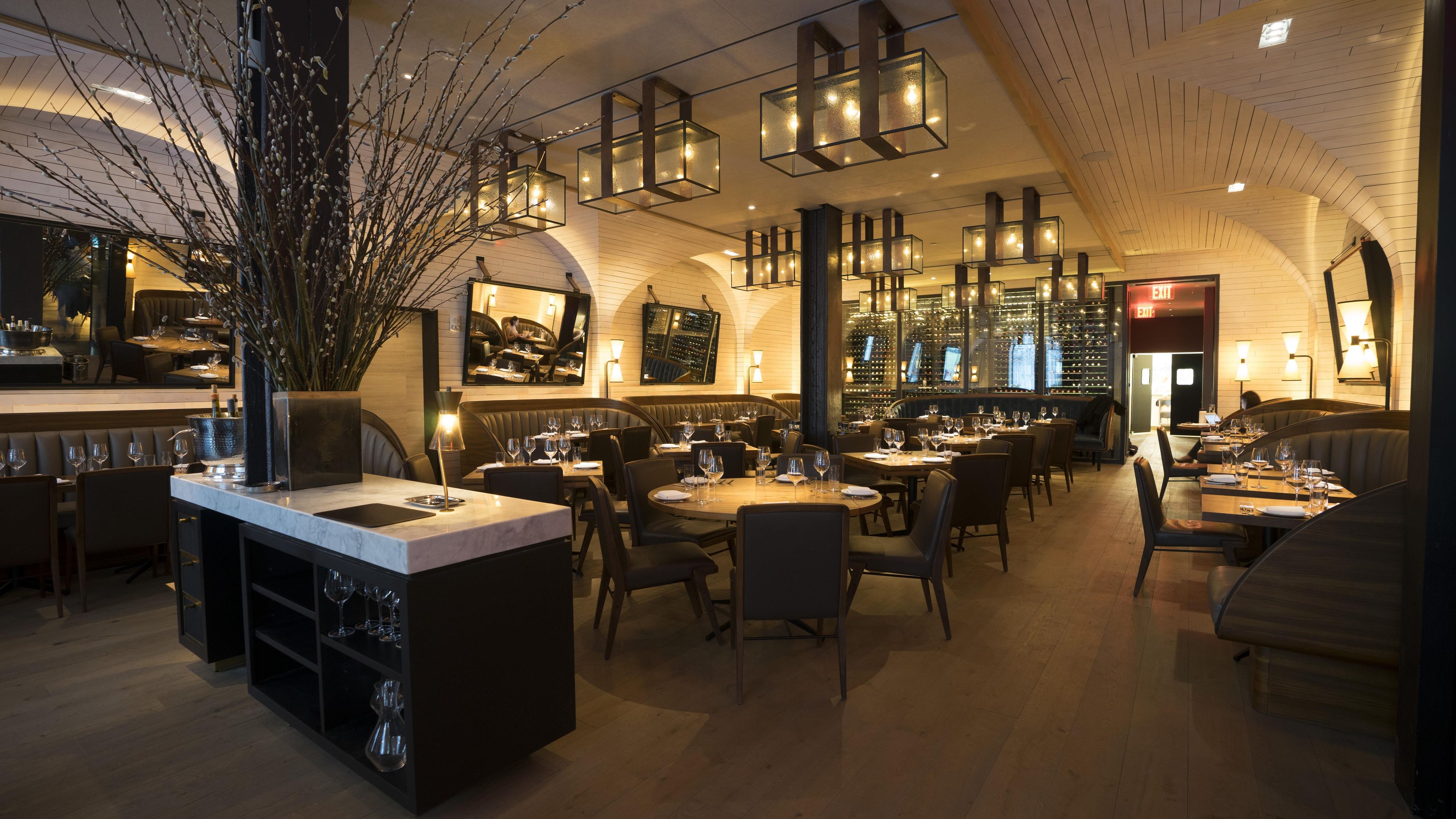 A restaurant with a bar area, multiple dining tables, and a wine rack.
