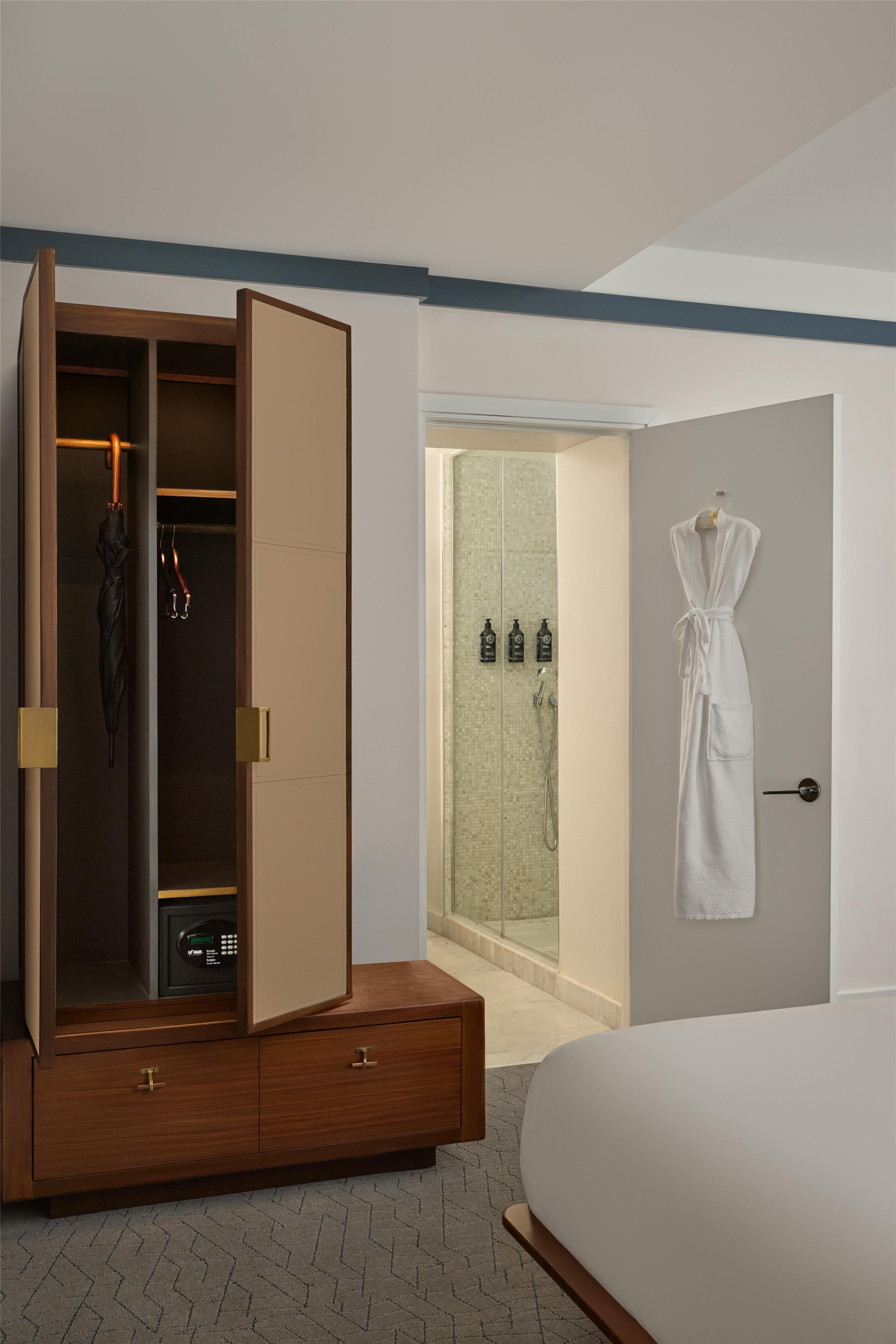 Une chambre avec une armoire en bois, un dressing, un espace douche et un peignoir blanc accroché au mur.