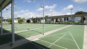 Una cancha de tenis con la señalización 'No caminar sobre las canchas', un área de estar techada y un cielo despejado.