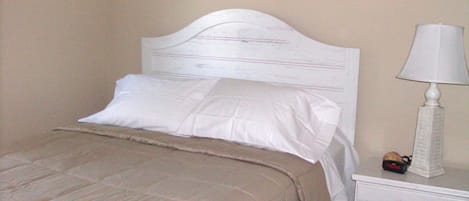 A neatly made bed with a white headboard and a beige bedspread.