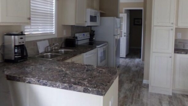 A compact kitchen with white cabinets, a granite countertop, a microwave, a stove, and a refrigerator. - Southern Charm RV Resort (Zephyrhills)
