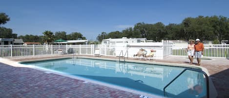 A swimming pool with a white fence, a clear sky, and trees in the background.