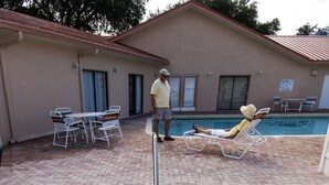 A swimming pool with a metal pole, lounge chairs, and a building in the background. - Southern Charm RV Resort (Zephyrhills)