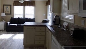 A compact kitchen with a built-in island, a dining area with a dark-colored sofa, and a ceiling fan. - Southern Charm RV Resort (Zephyrhills)