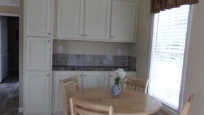 A dining area with a round wooden table, six chairs, and a vase with flowers. - Southern Charm RV Resort (Zephyrhills)